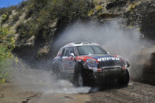 Mini Cooper drives through a puddle, forming splashes