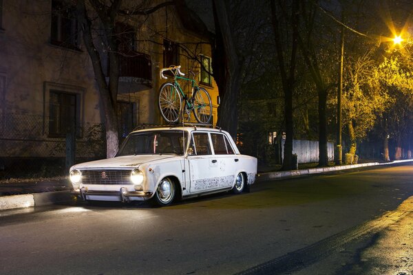 Une Lada blanche avec un vélo sur le toit attend le propriétaire la nuit