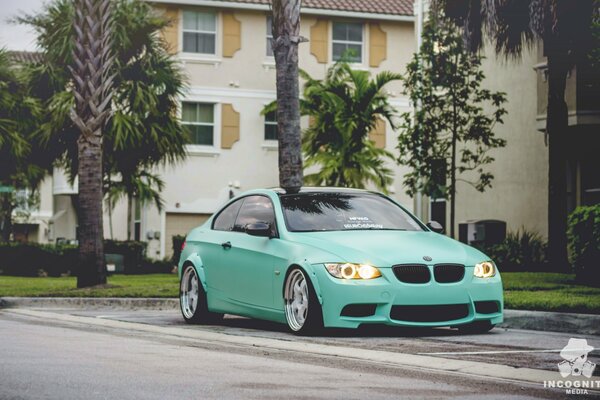 A green BMW 3 series is parked near the house