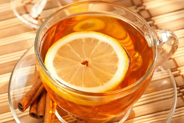 Thé dans une tasse transparente avec une tranche de citron et des bâtons de cannelle