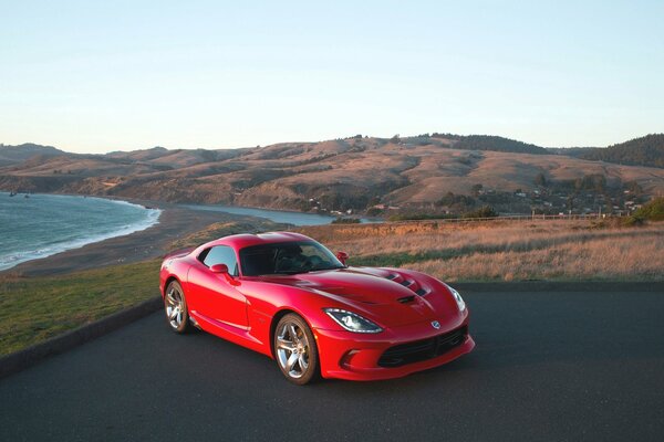 Red coupe car on the background of water and mountains