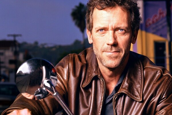 Hugh Laurie trägt eine Lederjacke auf einem Motorrad