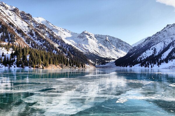 Lago ghiacciato, montagne coperte di neve, foresta sulle pendici delle montagne. Giornata di sole