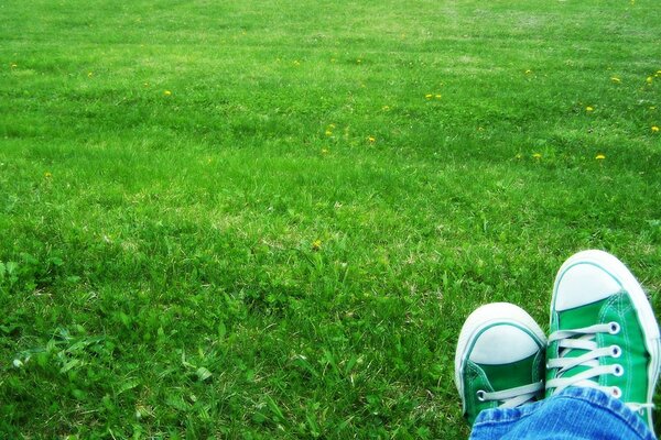 Feet in green sneakers lie on the grass