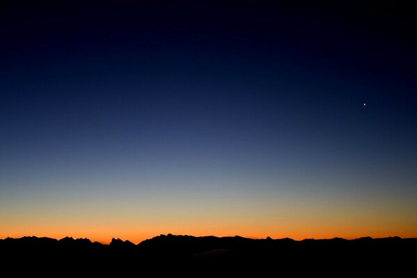 Una franja de horizonte negro contra el fondo de la línea naranja del sol naciente y el cielo azul que pasa a la noche