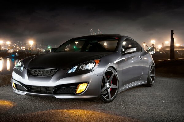 The Hyundai Genesis coupe car is on the street at night with the headlights on