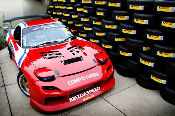 Red mazda rx- 7. moto tuning on the background of a wall of tires