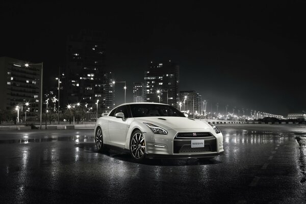 Nissan GT-R blanco sobre asfalto mojado en el fondo de la ciudad nocturna