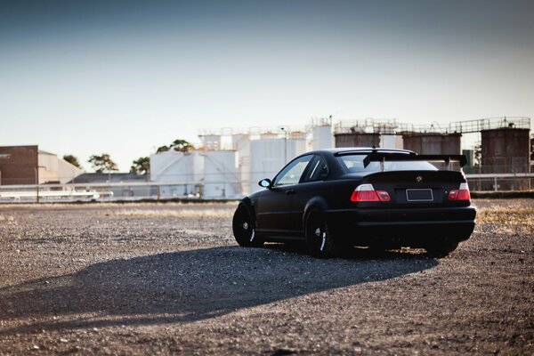 Matte black BMW with spoiler on the background of tanks