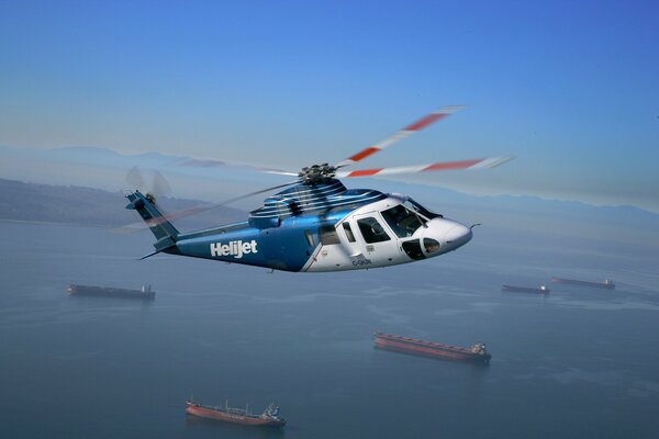 Синий вертолет s-76 в полете над океаном