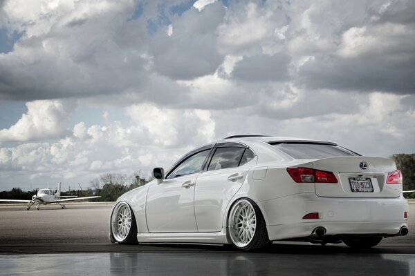 A white Lexus competes with an airplane against a cloudy sky
