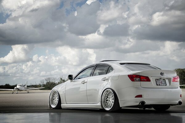 Un Lexus blanco compite con un avión contra un cielo nublado