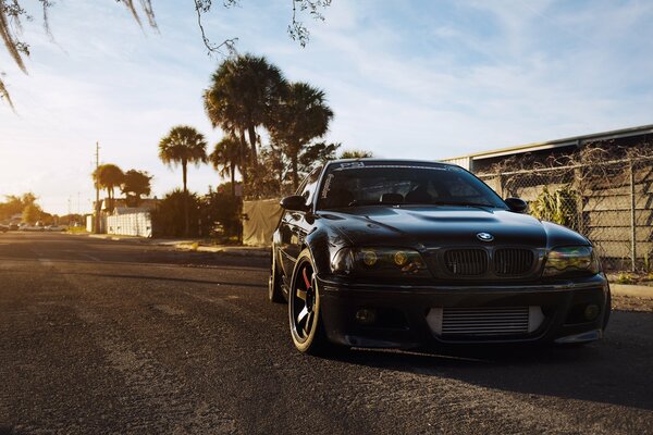 Frente de un BMW sintonizado al atardecer con árboles en el fondo