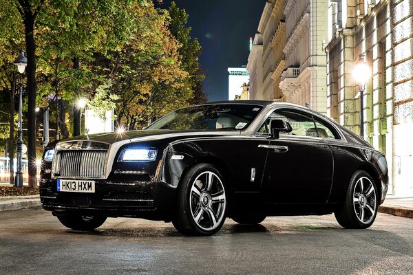 Rolls Royce in schwarzer Farbe auf der nächtlichen Straße der Stadt