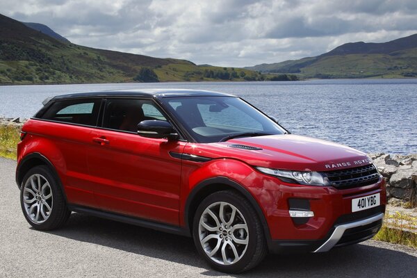 Coche rojo Land Rover en la orilla del lago