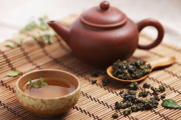 A small teapot with a cup of tea on a mat