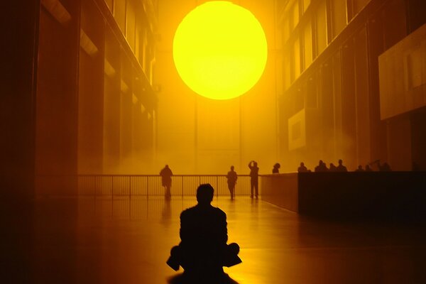 A man sits on the floor and looks at the giant sun