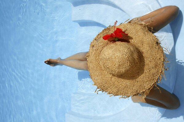 Chica con sombrero de paja sentada en la piscina