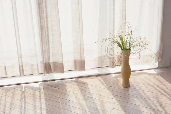 A vase of greenery in a room near a white curtain