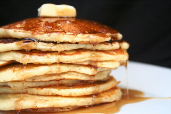 A stack of pancakes poured with honey on a white plate