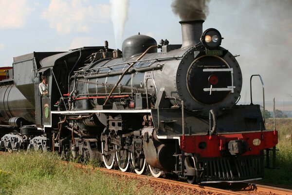 Schwarze Dampflokomotive rollt über die Schienen