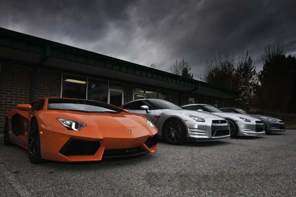 Autos der Marken Lamborghini, Aventador, Nissan vor dem Hintergrund des Gebäudes und des grauen Himmels in den Wolken