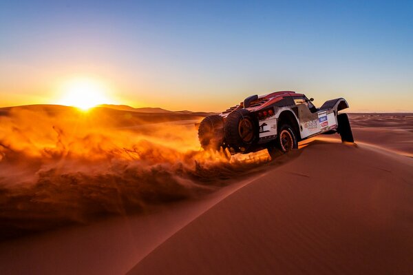 Une voiture roule sur le sable au coucher du soleil