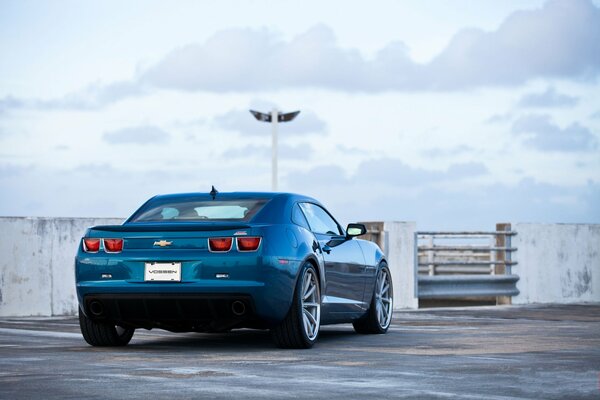 Blue chevrolet camaro ss in the parking lot in the middle of a white sky with white clouds floating on it