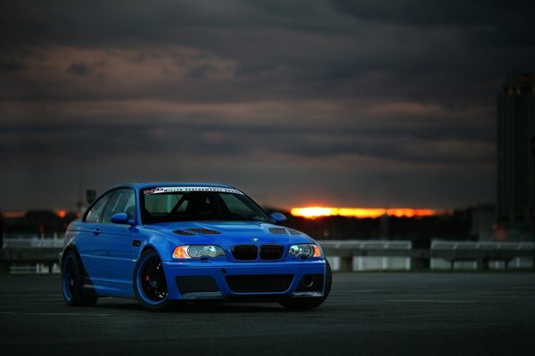 Blue BMW and sunset clouds behind