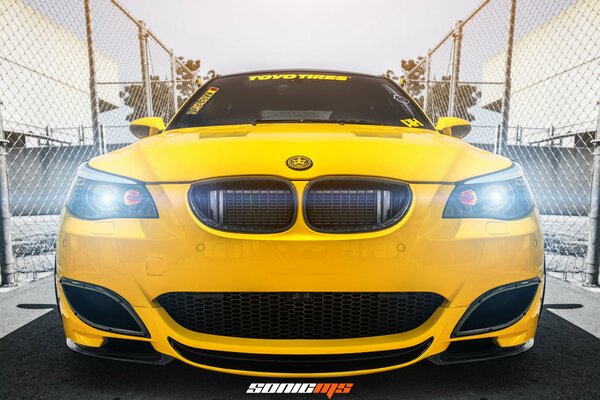 BMW m5 yellow between mesh fences