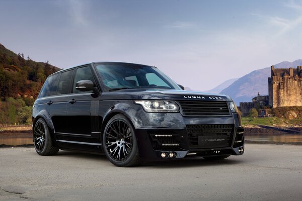 Schwarzer Range Rover vor dem Hintergrund der Berge und der alten Burg