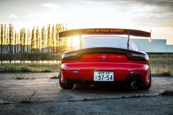 Rojo Mazda RX-7 con alerón vista trasera. En el fondo de la puesta de sol