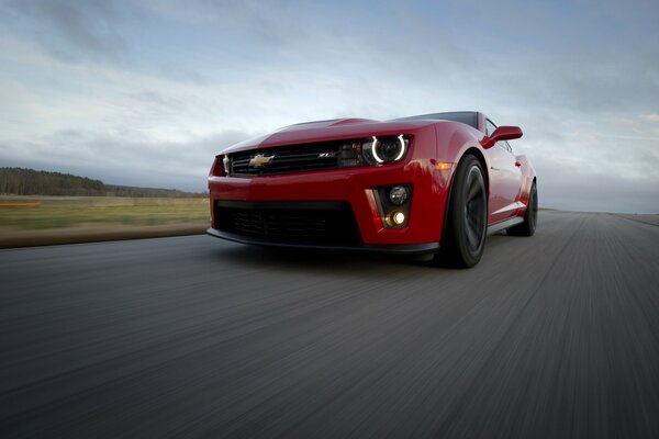 A red Chevrolet is driving at speed on the road