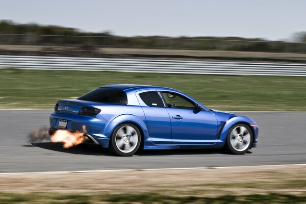 Una Mazda blu corre in pista con il fuoco dal tubo di scappamento