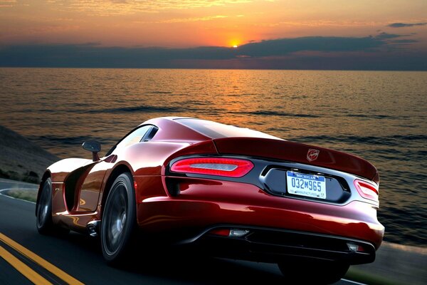 Red powerful Dodge Viper rides on the road against the background of the sea