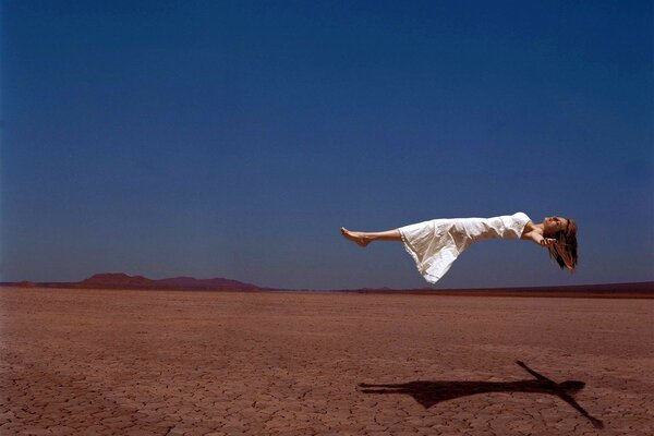 Chica con vestido blanco flotando sobre el desierto