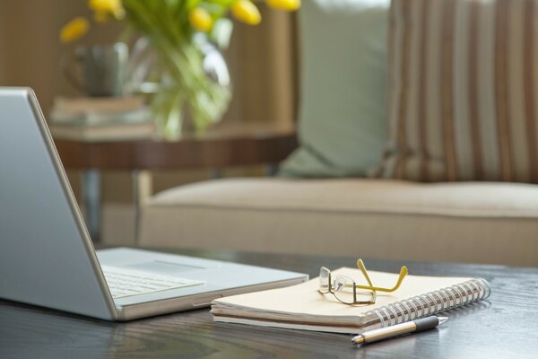 Auf dem Tisch steht ein Laptop mit Notizblock und Stift