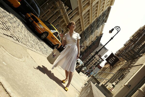 A girl in a white dress on the street in front of a taxi