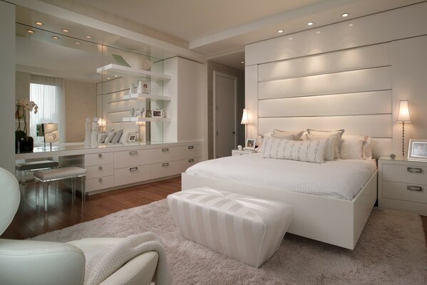Bedroom in white tones with a double bed, upholstered armchairs, carpet and chest of drawers