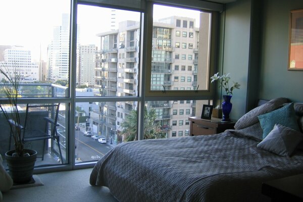 Schlafzimmer mit Fenster an der ganzen Wand, von dem aus die Stadt sichtbar ist