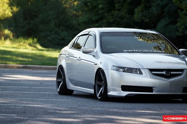 Une voiture acura tl de couleur blanche se tient près des arbres