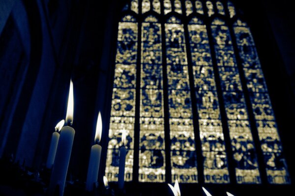 Dunkles Bild von Kerzen in der Kirche, große Glasfenster