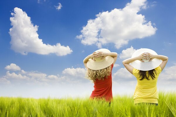 Image of two girls in hats in a field against a cloudy sky