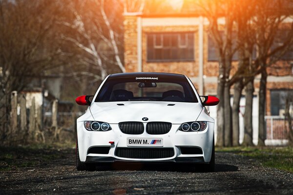 White bmw on the road against the background of trees and houses