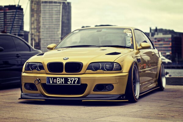 BMW M3 sintonizzata in oro sullo sfondo di edifici urbani