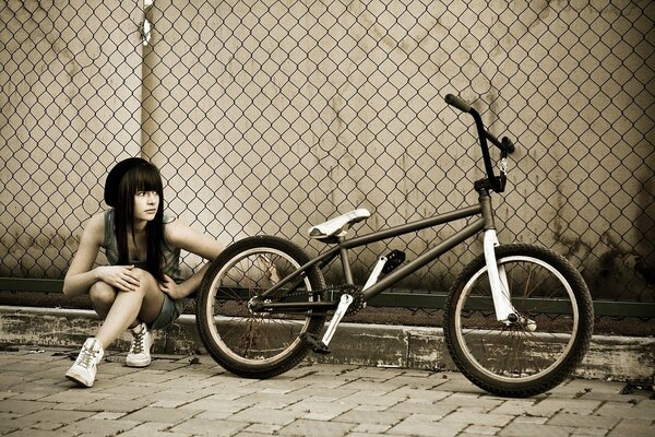 A girl with a bmx bike along a fence in a grid