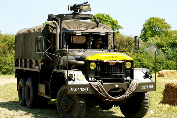 A large military truck with a driver on a background of green trees