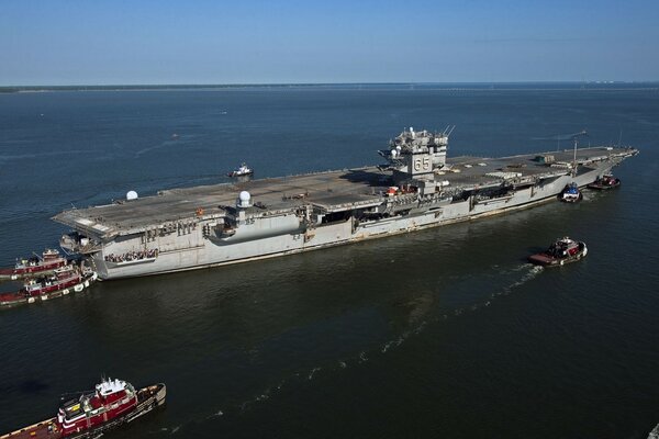 Small ships tow an aircraft carrier