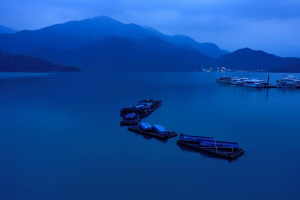 Un par de barcos se paran en la bahía por la noche contra el telón de fondo de las montañas y las luces de la orilla opuesta