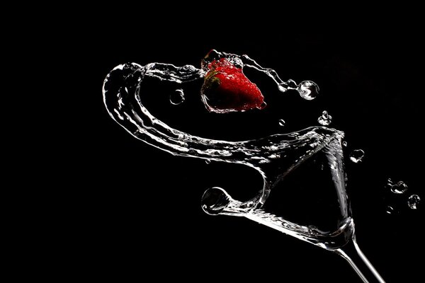 A spilled glass with water and strawberries on a black background